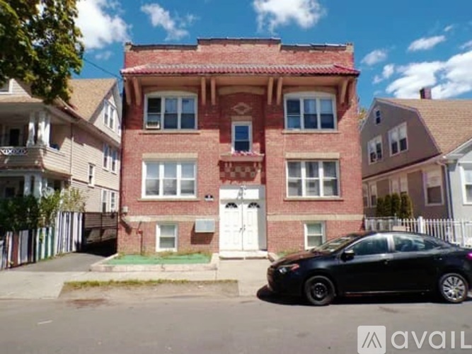 A black car is parked in front of a red brick house.