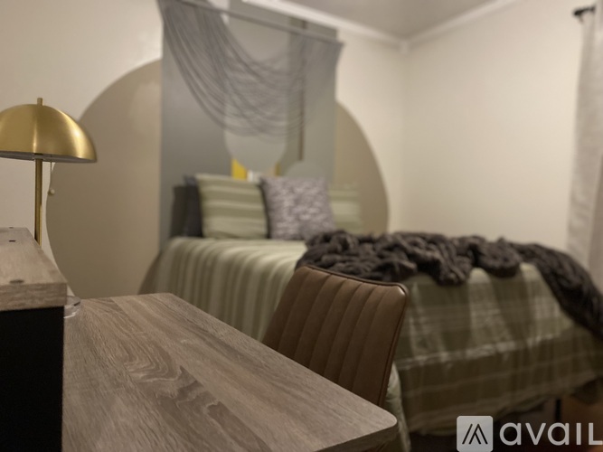 A bedroom with a bed covered in a grey blanket and a lamp on a wooden table.