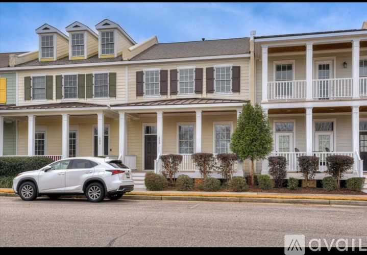 A white car is parked in front of a two-story building with a balcony.