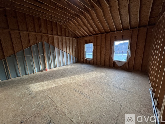 A spacious attic room with wooden walls and ceiling, and two windows letting in natural light.