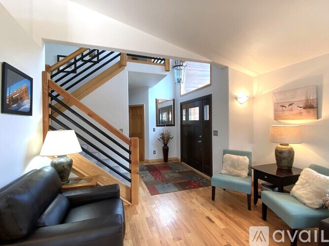A living room with a black leather couch and a wooden staircase.