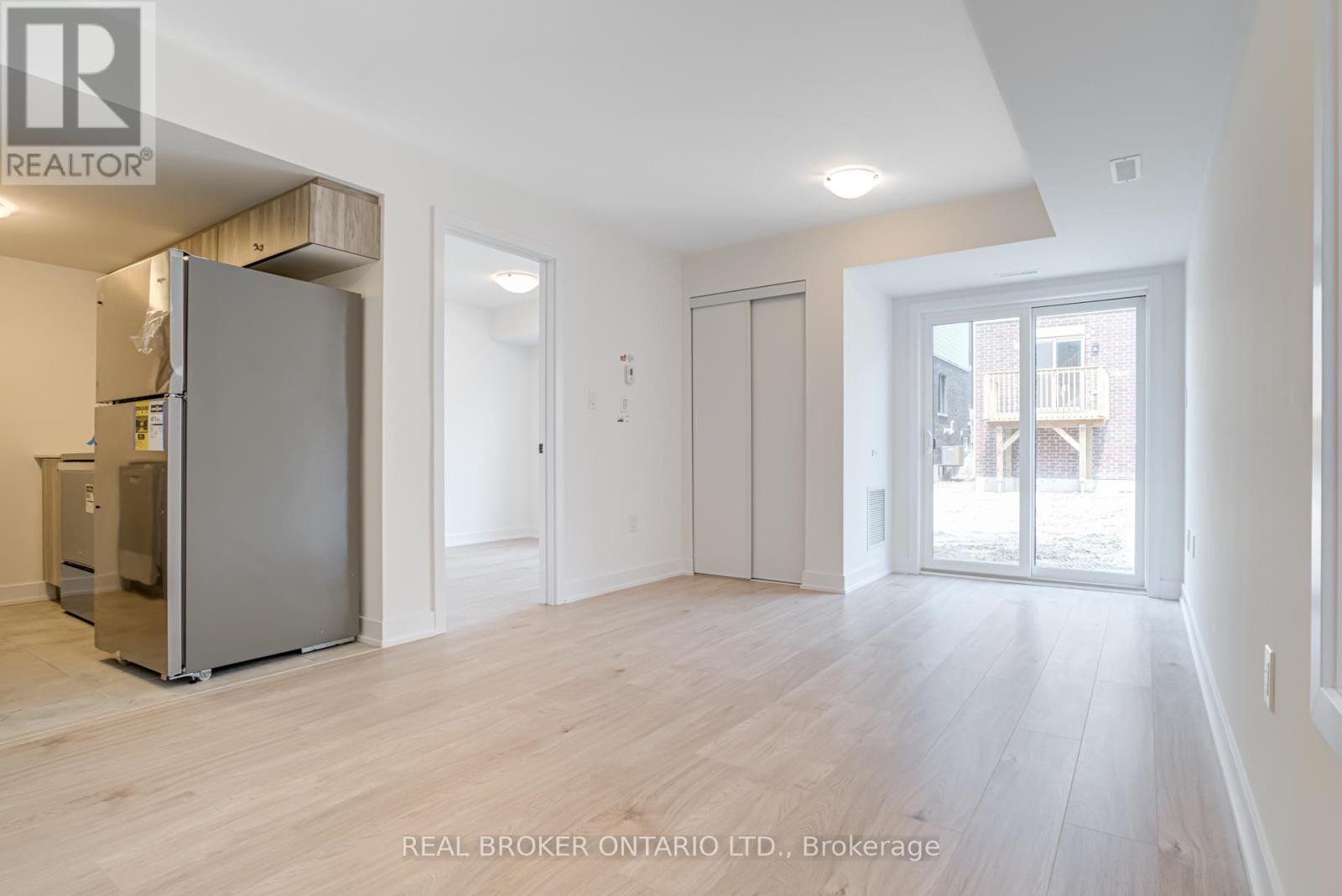 A spacious room with a grey fridge and wooden flooring.