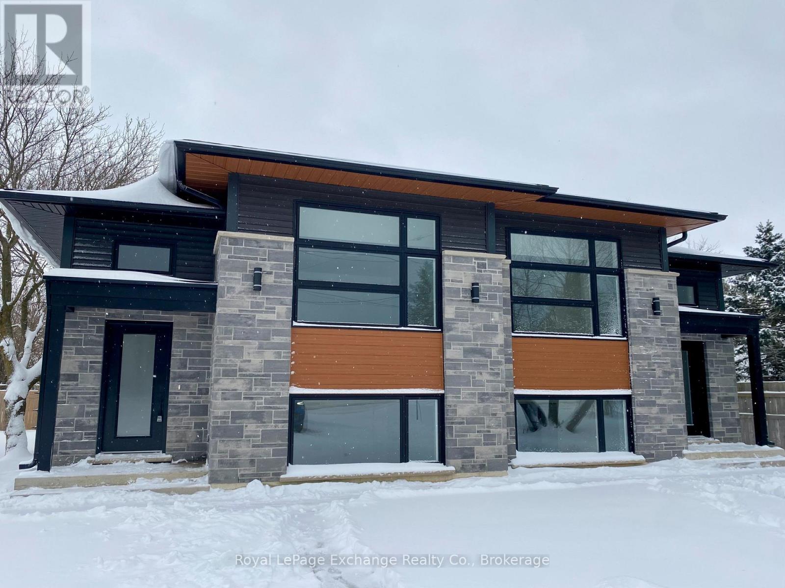 A modern house with a black and brown exterior is shown in the snow.