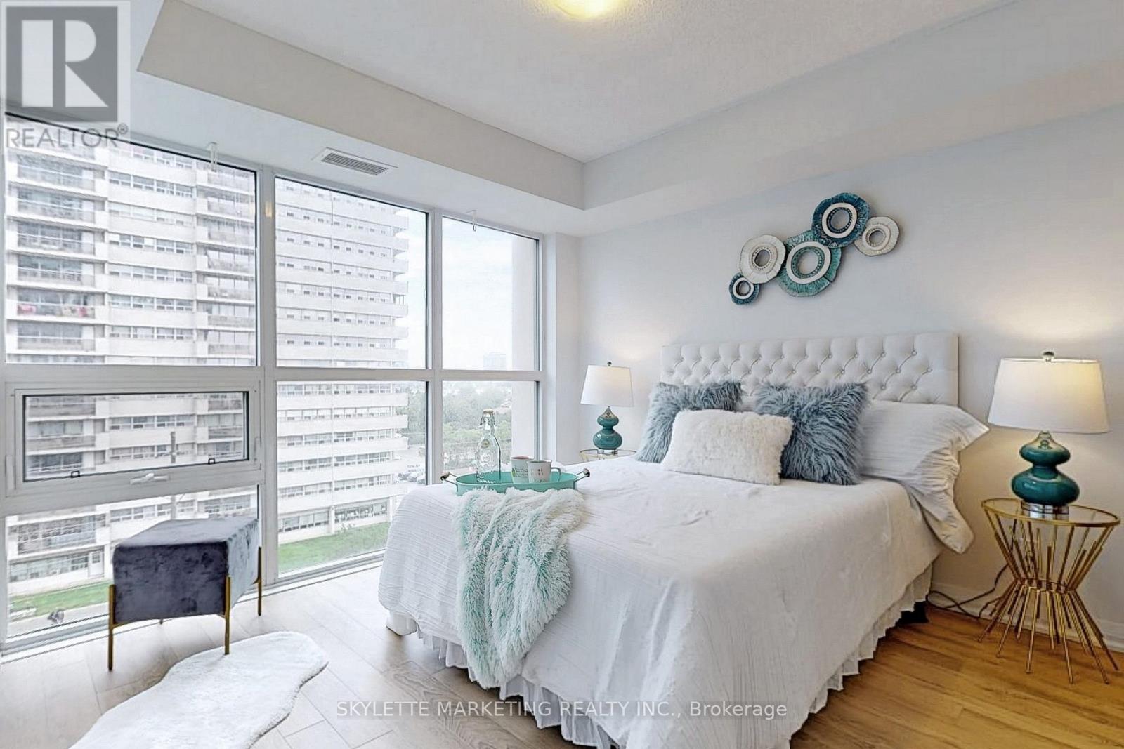A bedroom with a large bed and a balcony with a view of a parking lot.