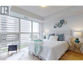 A bedroom with a large bed and a balcony with a view of a parking lot.