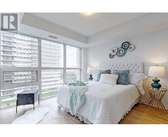 A bedroom with a large bed and a balcony with a view of a parking lot.