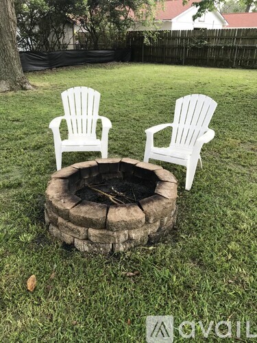 Two white chairs are placed around a fire pit in a grassy area.