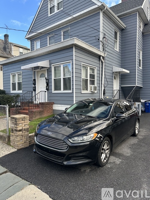 A black car is parked in front of a blue house.