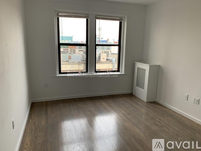 A room with a window overlooking a cityscape and a white refrigerator to the right.