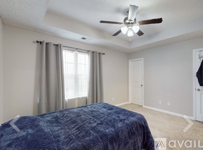 A bedroom with a bed, ceiling fan, and window with curtains.