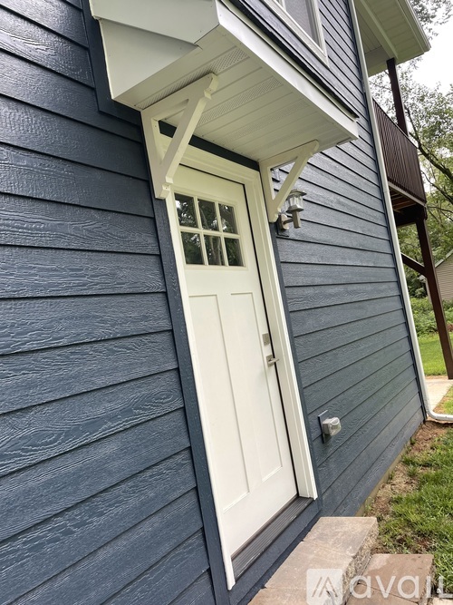 A white door with a window is on a blue house.
