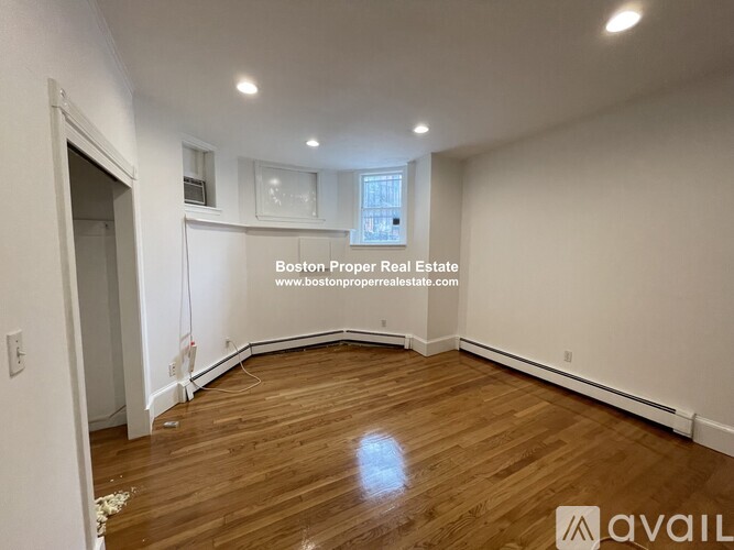 A room with wooden flooring and white walls, with a window and a door visible.