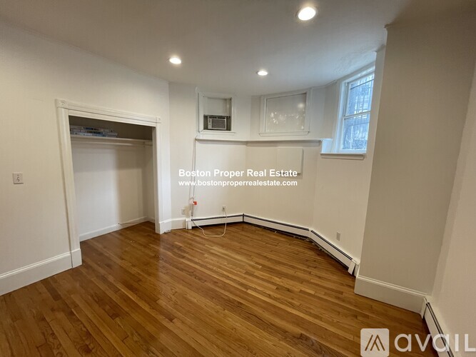 A room with wooden flooring and white walls, with a window on the right side.