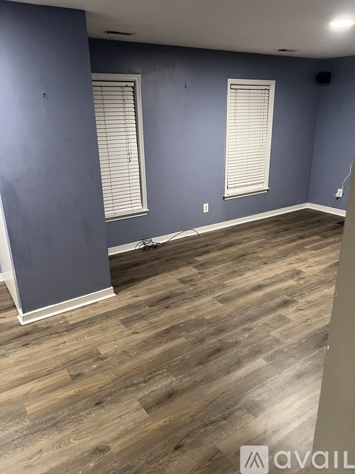 A room with wooden flooring and two windows with blinds.