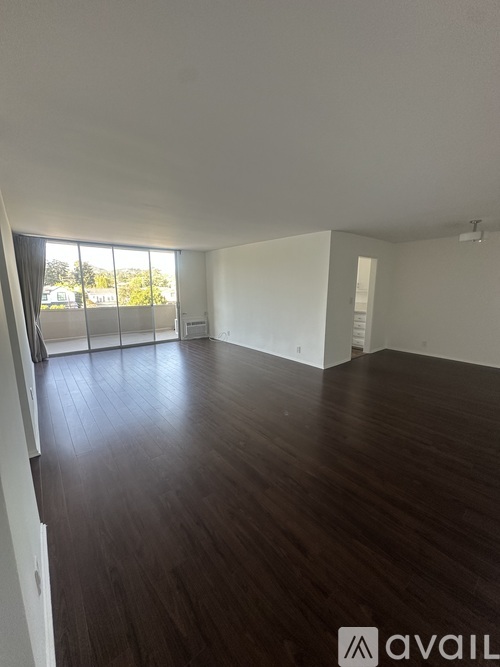 A spacious room with wooden flooring and large windows.