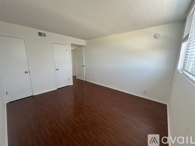 A room with wooden flooring and white walls with three doors.