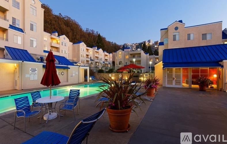 A pool area with chairs and a table with a red umbrella.