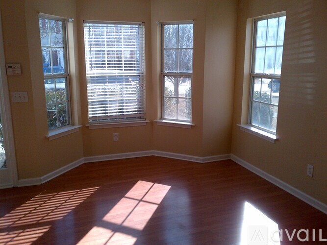 A room with wooden floors and three windows letting in sunlight.