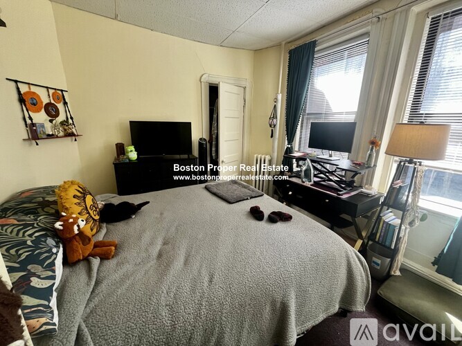 A bedroom with a bed, a desk with a computer, and a window with curtains.