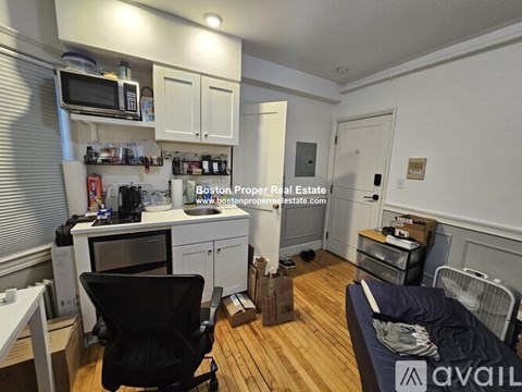 A small kitchen with a black chair and a bed in the corner.