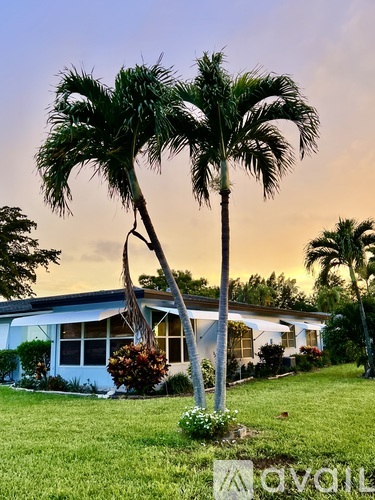 A house with a blue roof and white walls is surrounded by palm trees.