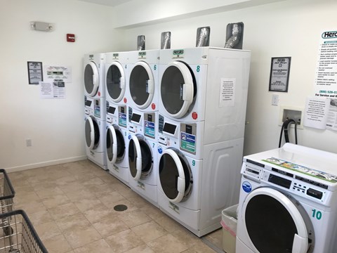 A row of white front load washing machines are lined up in a laundromat.