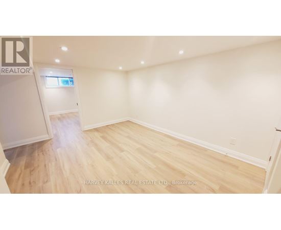 A spacious room with wooden flooring and white walls, featuring a kitchen area with cabinets and a window.