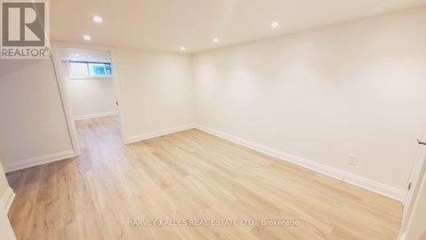 A spacious room with wooden flooring and white walls, featuring a kitchen area with cabinets and a window.