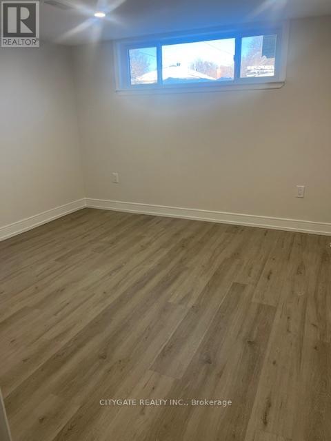 A room with wooden flooring and a window showing a view of trees and houses outside.