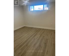 A room with wooden flooring and a window showing a view of trees and houses outside.
