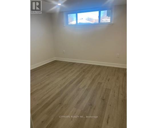 A room with wooden flooring and a window showing a view of trees and houses outside.