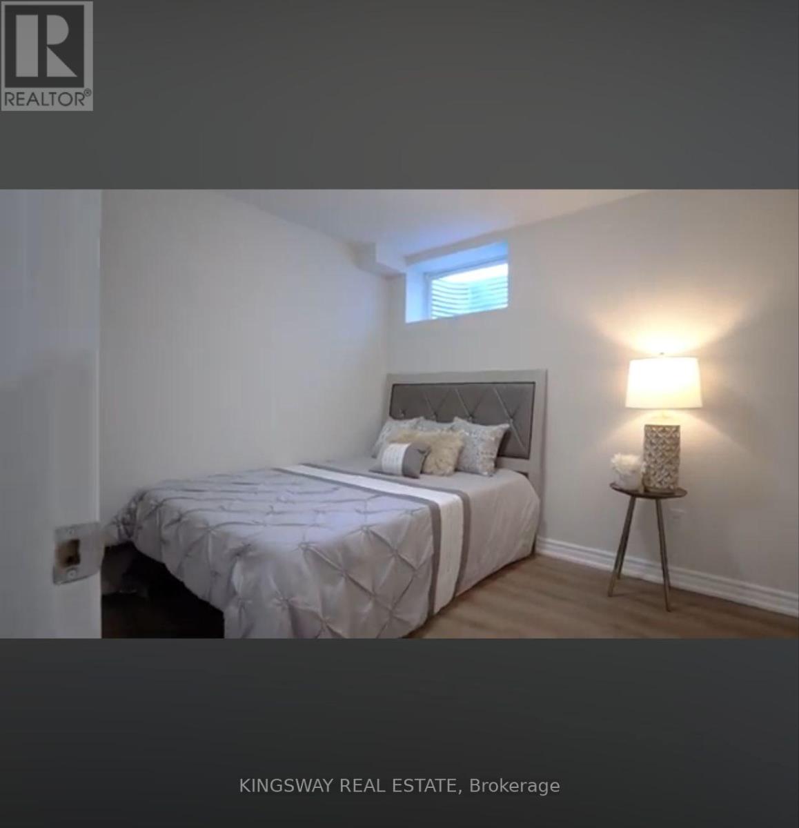 A bedroom with a bed, a small table with a lamp, and a window.