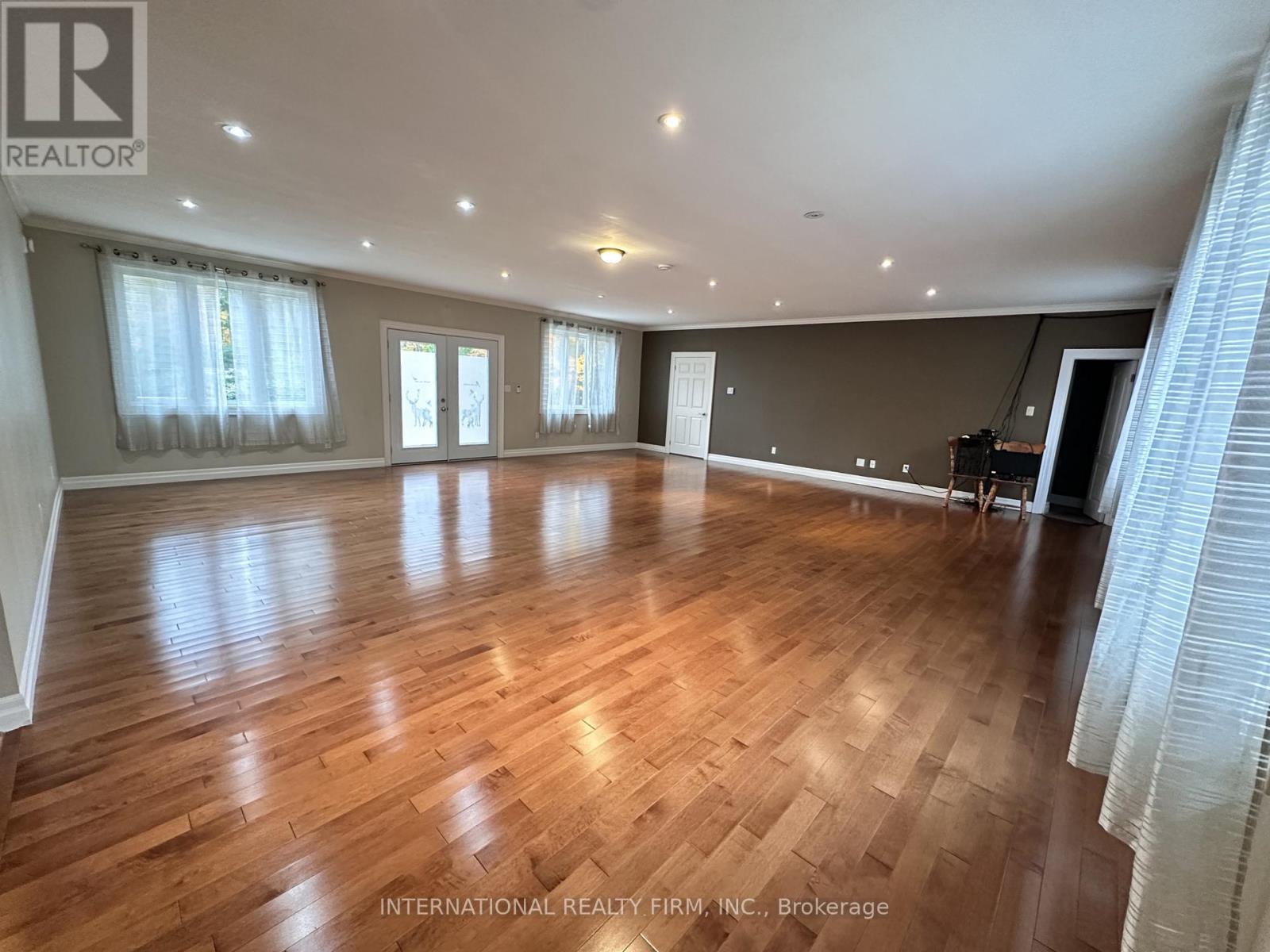 A spacious room with wooden flooring and large windows.