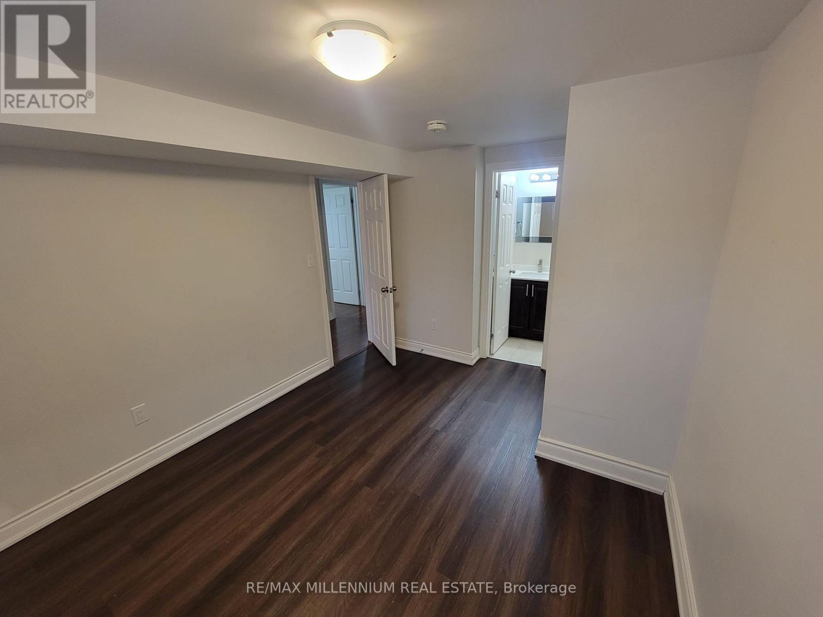 A room with wooden floors and white walls, with a door leading to another room.
