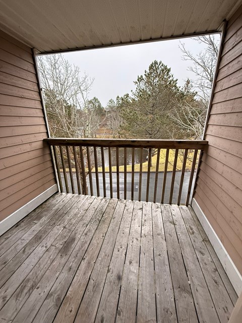 A wooden deck with a railing and a view of a grassy area.