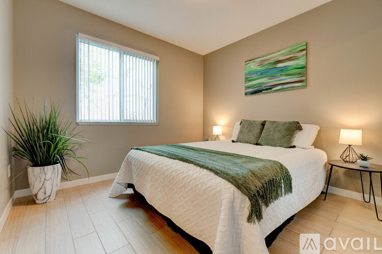 A bedroom with a bed, a potted plant, and a painting on the wall.