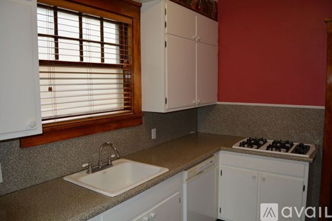 A kitchen with white cabinets and a window with blinds.