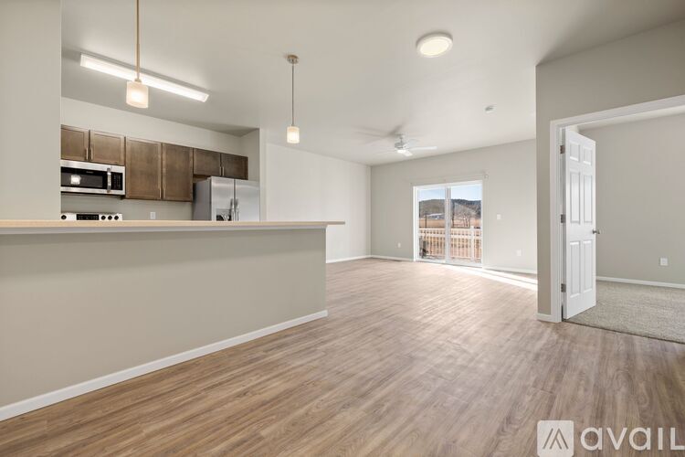 A spacious living room with wooden flooring and a kitchen area with brown cabinets.