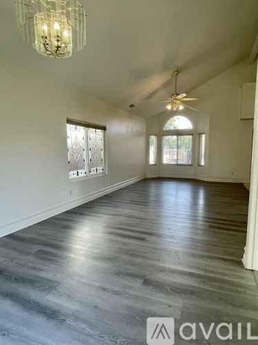 A spacious room with a chandelier, ceiling fan, and large windows.