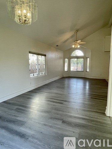 A spacious room with a chandelier, ceiling fan, and large windows.