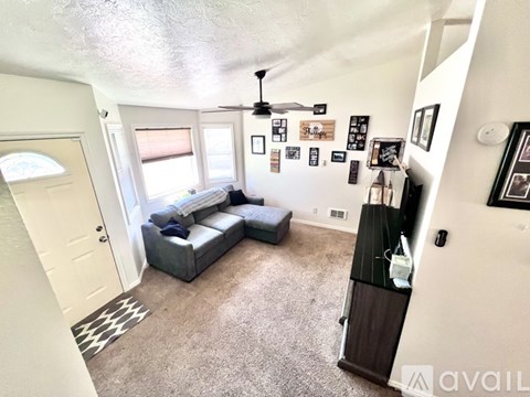 A living room with a grey couch and a fan on the ceiling.