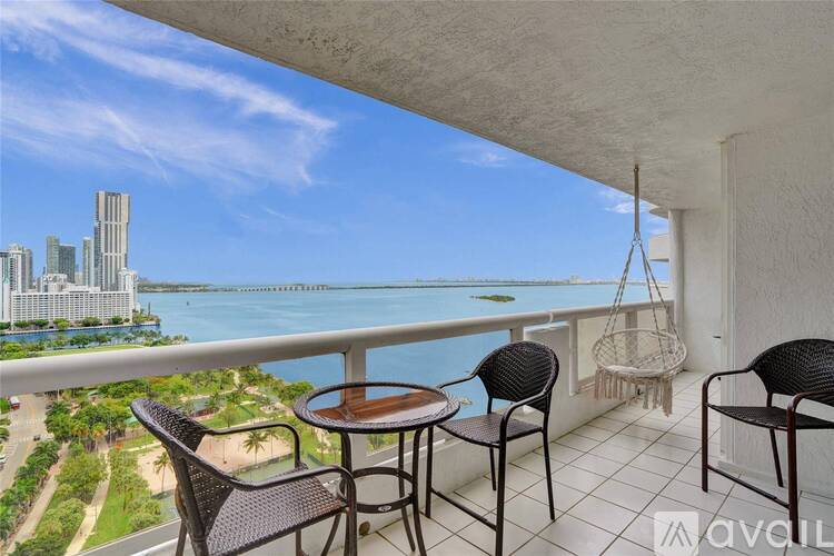 A balcony with a table and chairs overlooking a city skyline and water.