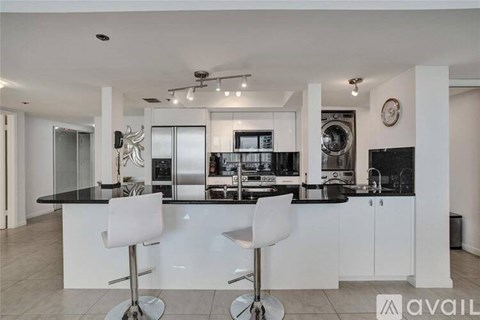 A modern kitchen with white chairs and black countertops.