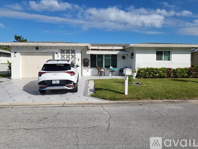A white car is parked in front of a house with a garage.