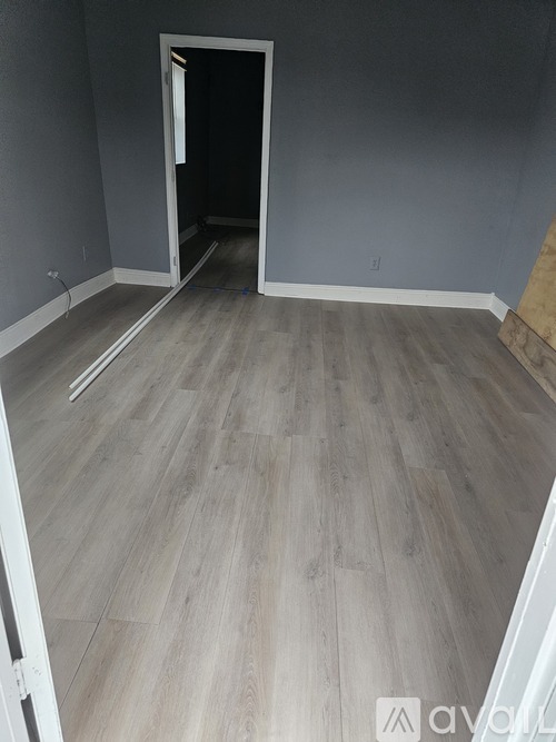 A room with wooden flooring and a doorway leading to another room.
