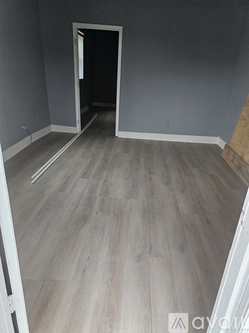 A room with a wooden floor and a doorway leading to another room.