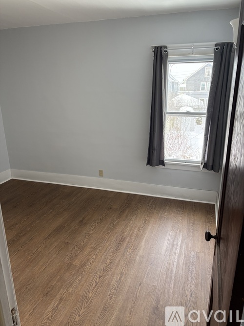 A room with wooden flooring and a window with black curtains.