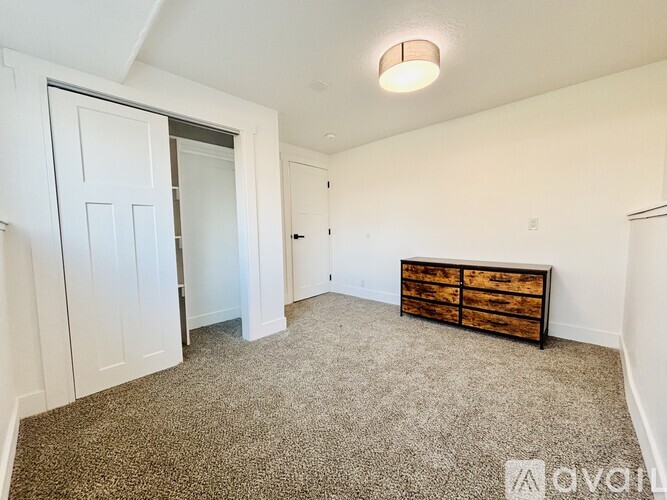 A room with a carpeted floor, a wooden chest of drawers, and a sliding door.