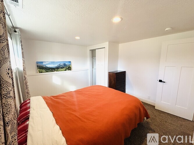 A bedroom with a bed, a painting on the wall, and a carpeted floor.
