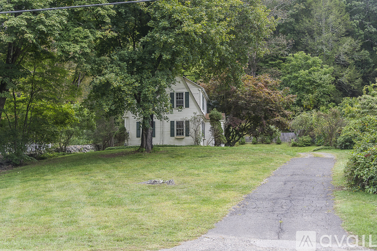 A house is surrounded by trees and a dirt road leads to the front door.